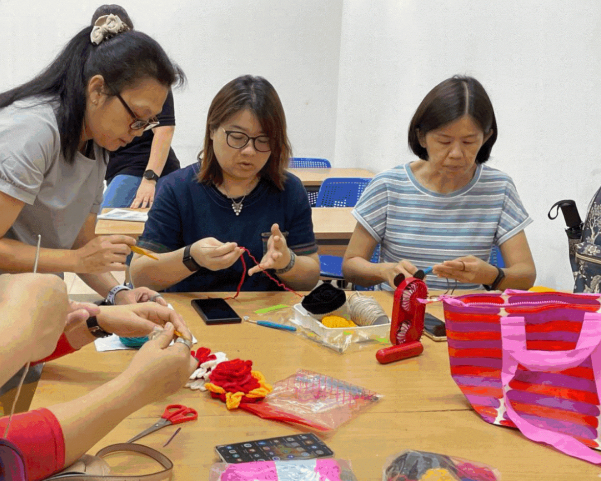 Participants learning crochet at a workshop, working with colourful yarn around a table with craft supplies.
